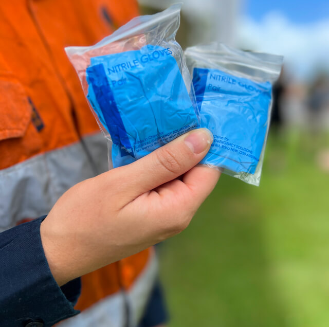 A person holding two sealed packets of nitrile gloves outdoors.