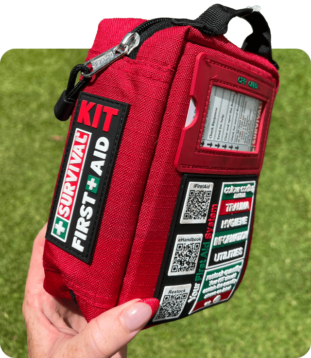 A hand holding a red first aid kit with survival instructions and labels.